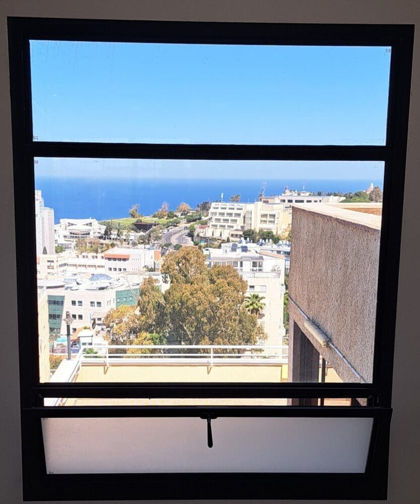 חלון שהוא מסגרת לנוף האורבני ובו "מצוירת" העיר חיפה – בבית נגה כרמי, בעלת ומנכ"ל אתר חי פה (צילום: רחלי אורבך)
