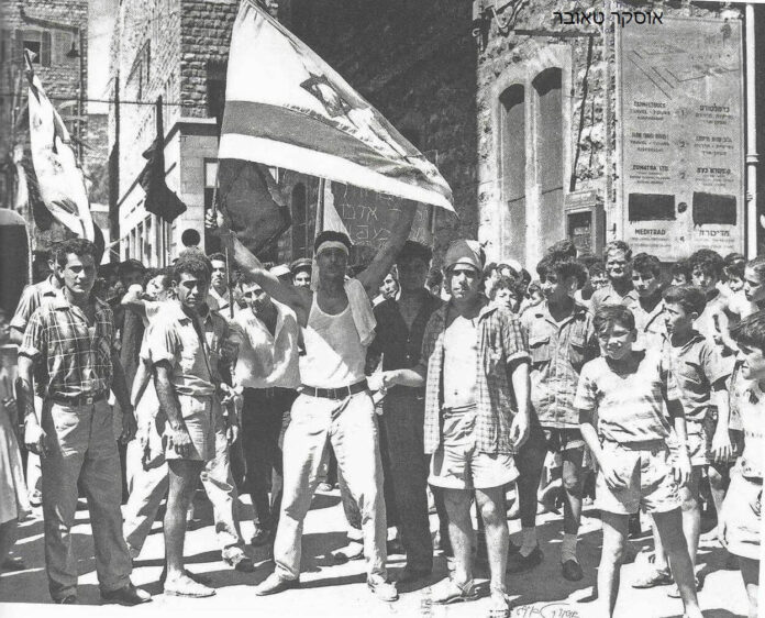 מפגין מניף דגל ישראל מוכתם בדם (9.7.1959) • צילום: אוסקר טאובר (*)