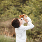 Child boy hugging kissing jack russell terrier puppy outdoors while walking with pet