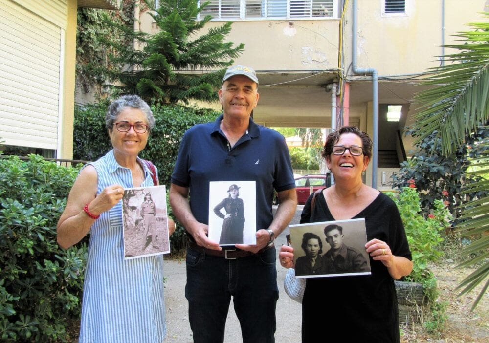 תמי וקנין ואורנה ודודו צור עם תמונות הוריהם במדים ברקע הבית בו גדלו בשיכון הבריגדה, 2017 (צילום: יעל הורוביץ)