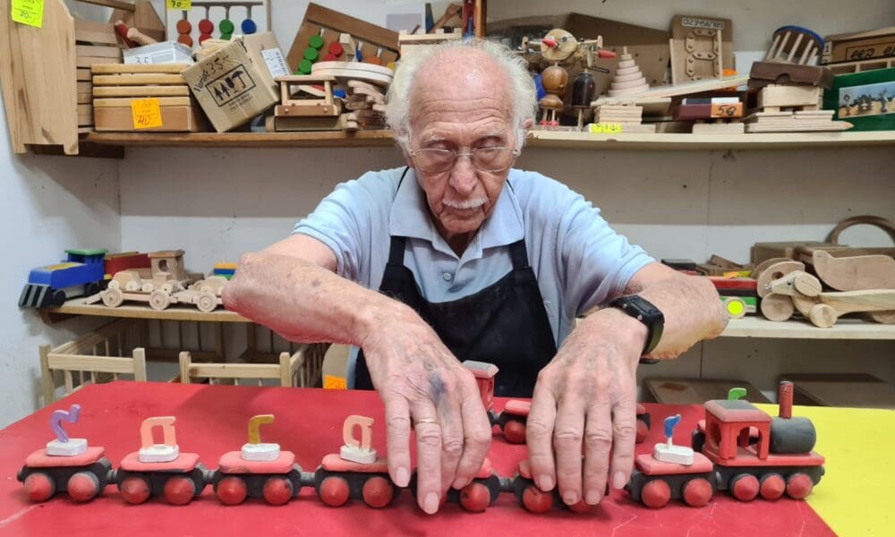 צבי עם אחד הצעצועים שבנה בנגרייה, רכבת עם אותיות מתחלפות (צילום: יעל הורוביץ)