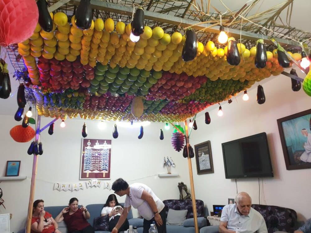 סוכת בית בשכונת השומרונים, חולון - סוכה תלויה מן התקרה, צבעונית, זוהרת ועמוסת פירות (צילום: רחלי אורבך)