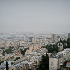 חיפה, נמל חיפה, מפרץ חיפה, הים התיכון, אוניות משא, ספינות, קו חוף, עיר חוף, נוף עירוני, מבנים, בניינים גבוהים, שכונות מגורים, אזור תעשייה, שמיים מעוננים, מזג אוויר חורפי, ערפל ימי, אובך, שמיים אפורים, זיהום אוויר, ראות נמוכה