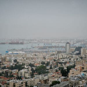 חיפה, נמל חיפה, מפרץ חיפה, הים התיכון, אוניות משא, ספינות, קו חוף, עיר חוף, נוף עירוני, מבנים, בניינים גבוהים, שכונות מגורים, אזור תעשייה, שמיים מעוננים, מזג אוויר חורפי, ערפל ימי, אובך, שמיים אפורים, זיהום אוויר, ראות נמוכה