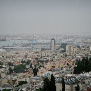 חיפה, נמל חיפה, מפרץ חיפה, הים התיכון, אוניות משא, ספינות, קו חוף, עיר חוף, נוף עירוני, מבנים, בניינים גבוהים, שכונות מגורים, אזור תעשייה, שמיים מעוננים, מזג אוויר חורפי, ערפל ימי, אובך, שמיים אפורים, זיהום אוויר, ראות נמוכה