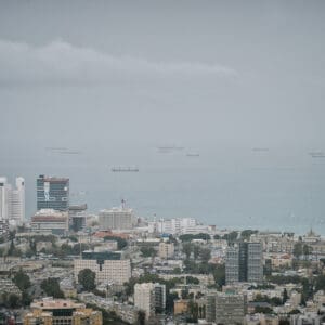 חיפה, נמל חיפה, מפרץ חיפה, הים התיכון, אוניות משא, ספינות, קו חוף, עיר חוף, נוף עירוני, מבנים, בניינים גבוהים, שכונות מגורים, אזור תעשייה, שמיים מעוננים, מזג אוויר חורפי, ערפל ימי, אובך, שמיים אפורים, זיהום אוויר, ראות נמוכה