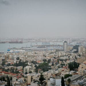 חיפה, נמל חיפה, מפרץ חיפה, הים התיכון, אוניות משא, ספינות, קו חוף, עיר חוף, נוף עירוני, מבנים, בניינים גבוהים, שכונות מגורים, אזור תעשייה, שמיים מעוננים, מזג אוויר חורפי, ערפל ימי, אובך, שמיים אפורים, זיהום אוויר, ראות נמוכה