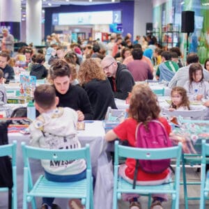אירוע צאו מהקופסה, טורניר משחקי קופסה, משחקי קופסה, אירוע משחקים, תחרות משחקים, אצטדיון סמי עופר, סמי עופר חיפה, חיפה, ישראל, אירוע בישראל, פעילות משפחתית, בילוי משפחתי, הורים וילדים, משפחות עם ילדים, ילדים משחקים, משחק חשיבה, משחק אסטרטגיה, משחק חברתי, משחק חינוכי, קהילה, אירוע קהילתי, תרבות ופנאי, חינוך בלתי פורמלי, למידה דרך משחק, שולחנות משחק, לוח משחק, קוביות משחק, קלפי משחק, בנייה בקוביות עץ, פאזל לילדים, פעילות לילדים, אינטראקציה חברתית, עבודת צוות, תחרות משפחתית, אולם אירועים, אירוע מקורה, קהל, אנשים משחקים, צילום אירועים, תרבות ישראלית, חוויית משחק, יצירתיות, פיתוח חשיבה, זמן איכות משפחתי