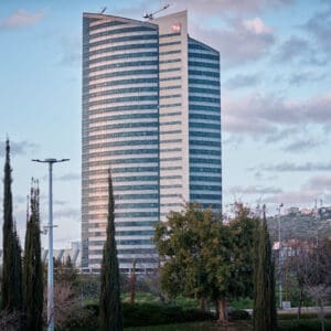 מטה חברת החשמל, מגדל חברת החשמל, בניין מה״ר חברת החשמל, מגדל משרדים, אדריכלות מודרנית, גורד שחקים, בניין זכוכית, משרדים גבוהים, תשתיות אנרגיה, משק החשמל בישראל, תשתיות לאומיות, חברה ממשלתית, מרכז ניהולי, אזור מת״מ חיפה, חיפה, ישראל, נוף עירוני חיפה, הר הכרמל ברקע, עצי ברוש, שטחים ירוקים, פיתוח עירוני, נדל״ן משרדי, מרכז עסקים, צילום אדריכלות, צילום אורבני, שקיעה בעיר, שמיים מעוננים, סביבה מודרנית, אזור תעסוקה, מגדל משרדים בישראל