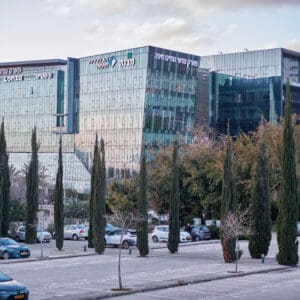 פארק מדעי החיים חיפה, פארק מת״מ, מת״מ חיפה, אזור הייטק חיפה, אצטדיון סמי עופר, חניון סמי עופר, מבני משרדים מודרניים, אדריכלות מודרנית, בניין זכוכית, גורדי משרדים, קמפוס הייטק, מרכז תעסוקה, חברות ביוטכנולוגיה, תעשיית מדעי החיים, תעשיית ההייטק בישראל, פיתוח עירוני, נדל״ן מסחרי, נוף עירוני חיפה, שקיעה עירונית, שמיים צבעוניים, רחוב עירוני, כלי רכב חונים, חניון פתוח, עצי נוי, ברושים, דקלים, שטחים ירוקים, תשתיות עירוניות, אזור עסקים, צילום אורבני, צילום אדריכלות, סביבה עירונית מודרנית, מרכז חדשנות, צמיחה כלכלית, אזור תעשייה מתקדמת, ישראל, חיפה