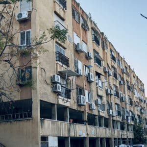 ואדי סליב, סאליב, בניין מגורים, שיכון ישן, חזית בטון, בנייה רוויה, שכונת מגורים, בניין דירות, מזגנים חיצוניים, מרפסות סגורות, תריסים, סורגים לחלונות, קירות מתקלפים, תשתיות חשופות, עמודי תמך, קומת עמודים, חניה פתוחה, רחוב עירוני, עץ בשלכת, שמיים מעוננים, אדריכלות ישראלית ישנה, צפיפות עירונית, נפתלי אימבר, שוק תלפיות