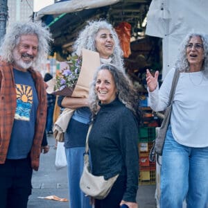 חברים בשוק, שוק תלפיות חיפה, מפגש חברתי, חיוך ושמחה, שיחה בין חברים, דיוקן רחוב, צילום רחוב, קניות בשוק, זר פרחים, חוויית שוק, קהילה מקומית, אווירה אורבנית, אנשים מבוגרים, שיער אפור מתולתל, אינטראקציה אנושית, רגע אותנטי, תרבות מקומית, רחוב עירוני, תאורה טבעית, תיעוד חברתישיער טבעי, שיער אפור טבעי, שיער לבן טבעי, שיער מתולתל טבעי, תלתלים כסופים, ללא צבע שיער, ללא החלקה, מראה טבעי, יופי טבעי, הזדקנות טבעית, קבלה עצמית, סגנון אישי, אותנטיות, מרקם שיער טבעי, דיוקן רחוב, צילום טבעי