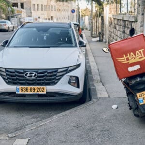 קטנוע משלוחים, שליח על קטנוע, רוכבי קטנוע, HAAT חיפה, אפליקציית משלוחים, משלוחי אוכל, שליח עירוני, לוגו HAAT, קופסת משלוחים אחורית, תחבורה דו גלגלית, תנועה עירונית, רחוב בחיפה, שירות מהיר,כלכלה, שליח עצמאי, סצנה אורבנית, חיי עיר, צילום רחוב, תיעוד יומיומי