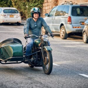 הסטורי, נוסטלגי, אופנוע וינטג׳, אופנוע עם סירה צדדית, רכב אספנות, רוכב אופנוע, קסדה פתוחה, משקפי מגן, נסיעה עירונית, כלי רכב קלאסי, מנוע ישן, מתכת ירוקה, סירה צד, תחבורה דו גלגלית, כביש עירוני, חובבי אופנועים, תחביב מוטורי, סגנון רטרו, רכב היסטורי, צילום תנועה, דינמיקה בכביש