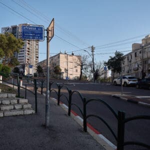 כביש ריק, רחוב שומם, עיר ריקה, היעדר תנועה, חירום לאומי, מצב חירום, מבצע שאגת הארי, מתיחות ביטחונית, עורף אזרחי, שגרה מופרעת, תחנת אוטובוס ריקה, תחבורה ציבורית מושבתת, בנייני מגורים ישנים, מגדל מגורים חדש, התחדשות עירונית, פינוי בינוי, שכונה ותיקה, שמיים בהירים, יום שמשי, תשתיות עירוניות, כביש עירוני, סימוני דרך, מדרכה ריקה, דממה עירונית, שקט מתוח, חזיתות מבנים, צילום תיעודי, צילום עיתונאי, מציאות ביטחונית בישראל, תמ״א 38, הריסה ובנייה מחדש, חיזוק מבנים, שדרוג תשתיות, בנייה רוויה, צפיפות עירונית, תכנון עירוני, מדיניות דיור, התחדשות שכונות ותיקות, פיתוח עירוני, שינוי ייעוד קרקע, הגדלת זכויות בנייה, שימור מול פיתוח, חידוש חזיתות, שיפור איכות חיים, השקעות נדל״ן, עליית ערך נכסים, פרויקטים למגורים, שיתוף דיירים, פיצוי דיירים, יזמות נדל״ן, רגולציה תכנונית, היתרי בנייה, ועדות תכנון ובנייה, שיקום מבנים ישנים, התחדשות תשתיות עירוניות, התחדשות מרכזי ערים, בנייה לגובה, בניין מגורים ישן, שיכון, בלוק דירות, חזית בניין, ארכיטקטורה ישראלית, שכונת מגורים, עיר ישראלית, רחוב עירוני, תחנת אוטובוס, תחבורה ציבורית, תחנת המתנה, עץ אורן, צמחייה עירונית, מדרכה, אבני סלע, כביש רטוב, שמש חזקה, שמיים כחולים, אור וצל, חזית מוזנחת, תריסים סגורים, מזגנים חיצוניים, אנטנות על הגג, צילום רחוב, סביבה עירונית, דיור ציבורי, מבנה בטון, נוף עירוני