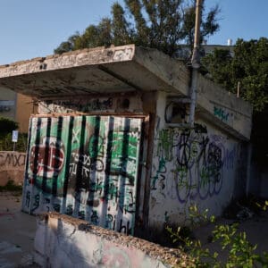 פינוי בינוי, התחדשות עירונית, תמ״א 38, הריסה ובנייה מחדש, חיזוק מבנים, שדרוג תשתיות, בנייה רוויה, צפיפות עירונית, תכנון עירוני, מדיניות דיור, התחדשות שכונות ותיקות, פיתוח עירוני, שינוי ייעוד קרקע, הגדלת זכויות בנייה, שימור מול פיתוח, חידוש חזיתות, שיפור איכות חיים, השקעות נדל״ן, עליית ערך נכסים, פרויקטים למגורים, שיתוף דיירים, פיצוי דיירים, יזמות נדל״ן, רגולציה תכנונית, היתרי בנייה, ועדות תכנון ובנייה, שיקום מבנים ישנים, התחדשות תשתיות עירוניות, התחדשות מרכזי ערים, בנייה לגובה, בניין מגורים ישן, שיכון, בלוק דירות, חזית בניין, ארכיטקטורה ישראלית, שכונת מגורים, עיר ישראלית, רחוב עירוני, תחנת אוטובוס, תחבורה ציבורית, תחנת המתנה, עץ אורן, צמחייה עירונית, מדרכה, אבני סלע, כביש רטוב, שמש חזקה, שמיים כחולים, אור וצל, חזית מוזנחת, תריסים סגורים, מזגנים חיצוניים, אנטנות על הגג, צילום רחוב, סביבה עירונית, דיור ציבורי, מבנה בטון, שכונה ותיקה, נוף עירוני, קיוסק, נוסטלגיה, מורשת, הזנחה