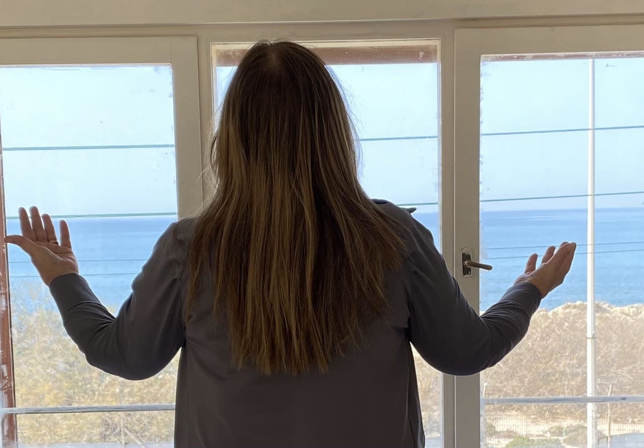 אישה מול חלון מרימה ידיים לתפילה ותקווה (צילום: חנה מורג)