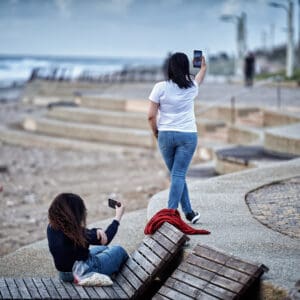 חוף ים, טיילת, חיפה, חוף הכרמל, ים סוער, גלים, שמיים דרמטיים, עננים, חורף, חוף סלעי, חול, קו חוף, מבנה הצלה, סככת חוף, נוף עירוני, קו אופק, צילום נוף, צילום חוף, שקמונה, נשים צעירות, סמארטפון, צילום, סלפי, טיילת חוף, ישיבה, ספסל, הליכה, צילום רחוב, חוף ים, בת גלים חיפה, רגע יומיומי, lifestyle, טיילת, טלפון נייד, רשת חברתי