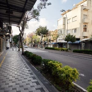 רחוב הרצל, רחוב יחיאל, הדר הכרמל, מסחר, חנויות, תריסי גלילה, מדרכה, ריצוף, כביש, שלטי רחוב, תמרורים, מגדל חיפה, בנייני מגורים, צמחייה עירונית, עצי סיגלון, פריחה סגולה, בובת תצוגה, פח אשפה, גרפיטי, שלטי השכרה, נוף עירוני, תשתיות