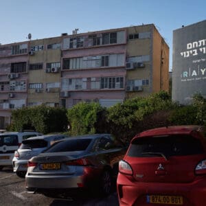 פינוי בינוי, התחדשות עירונית, תמ״א 38, הריסה ובנייה מחדש, חיזוק מבנים, שדרוג תשתיות, בנייה רוויה, צפיפות עירונית, תכנון עירוני, מדיניות דיור, התחדשות שכונות ותיקות, פיתוח עירוני, שינוי ייעוד קרקע, הגדלת זכויות בנייה, שימור מול פיתוח, חידוש חזיתות, שיפור איכות חיים, השקעות נדל״ן, עליית ערך נכסים, פרויקטים למגורים, שיתוף דיירים, פיצוי דיירים, יזמות נדל״ן, רגולציה תכנונית, היתרי בנייה, ועדות תכנון ובנייה, שיקום מבנים ישנים, התחדשות תשתיות עירוניות, התחדשות מרכזי ערים, בנייה לגובה, בניין מגורים ישן, שיכון, בלוק דירות, חזית בניין, ארכיטקטורה ישראלית, שכונת מגורים, עיר ישראלית, רחוב עירוני, תחנת אוטובוס, תחבורה ציבורית, תחנת המתנה, עץ אורן, צמחייה עירונית, מדרכה, אבני סלע, כביש רטוב, שמש חזקה, שמיים כחולים, אור וצל, חזית מוזנחת, תריסים סגורים, מזגנים חיצוניים, אנטנות על הגג, צילום רחוב, סביבה עירונית, דיור ציבורי, מבנה בטון, שכונה ותיקה, נוף עירוני