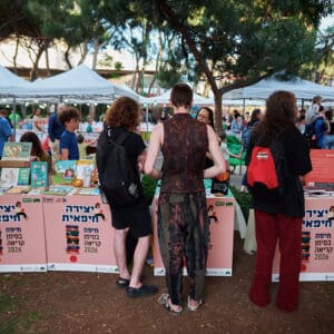 יריד, ספרים, דוכנים, קהל, אנשים, גן, עצים, תאורה, דמדומים, שקיעה, תרבות, אירוע, חוץ, הליכה, יצירה חיפאית, עמידה, התקהלות, חשיפה, צפיפות, חיפה, שלטים, ערב, שבוע הספר, גן האם