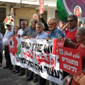 הפגנה, מחאה, שלטים, דגלים, דגל ישראל, נאום, נואם, במה, מיקרופון, קהל, אנשים, רחוב, מבנים, עצים, כיכר, צעדת מחאה, כרזות, פוליטיקה, אקטיביזם, התקהלות, פלסטין, פלסטינים, כיבוש, 1967, עימות