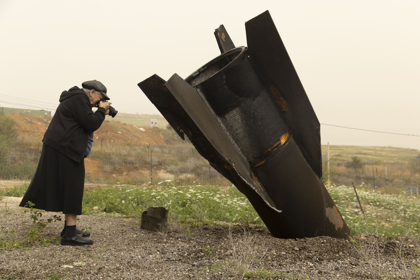 אמיר לוי, אישה מצלמת חלק של טיל שנורה מאיראן שנפל סמוך לרפת בשדמות מחולה שבבקעת הירדן, 3.4.2026 (צילום: מוזיאוני חיפה)